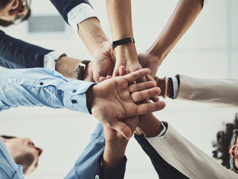Teamwork, collaboration and unity between business people with their hands stacked for project development and innovation. Group of corporate colleagues united, joining or working together from below.